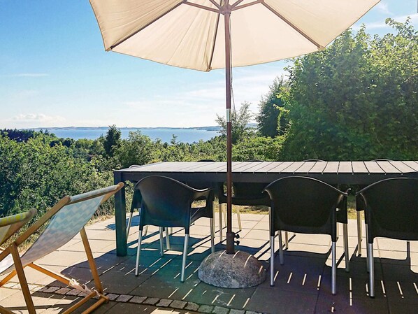 An outdoor patio with a table and chairs, a large umbrella, and a view of the sea.