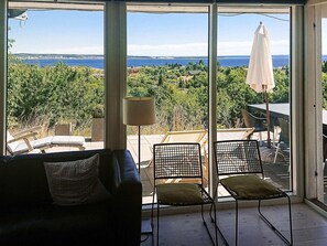 A room with a view of the sea, a sofa, two chairs, and a lamp.