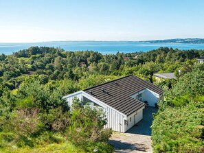 A cabin with a sloped roof, surrounded by dense greenery and a view of the water.