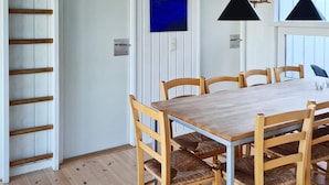 Un coin repas avec une table et des chaises en bois, un plancher en bois et un mur blanc orné d’une œuvre d’art bleue.