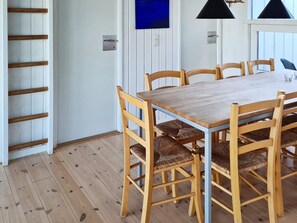 A dining area with a wooden table and chairs, a wooden floor, and a white wall with a blue artwork.