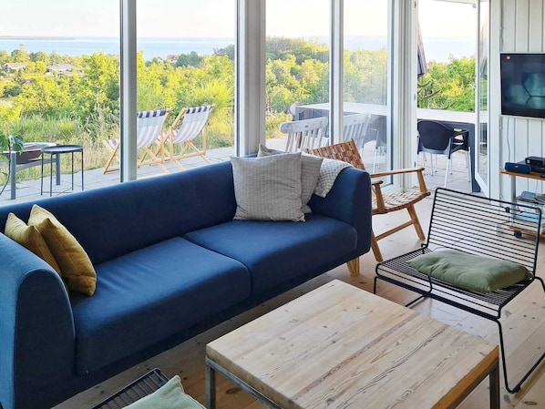 A modern living room with a blue sofa, a wooden coffee table, and a view of a forest and water.