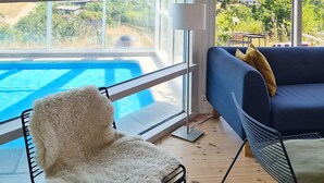Une pièce avec vue sur une piscine, un canapé bleu avec des coussins, un fauteuil moelleux et une chaise à armature métallique.