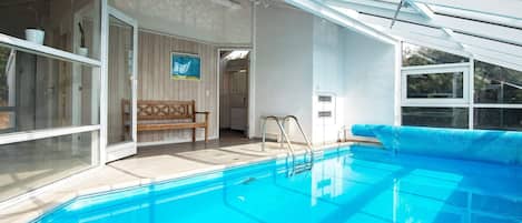 Ein Schwimmbecken mit einer Holzbank und einer Tür zu einem überdachten Bereich.