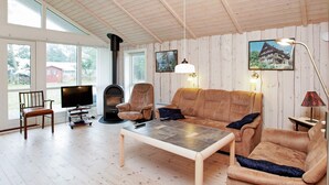 A cozy living room with a fireplace, comfortable seating, and large windows offering a view of the outdoors.