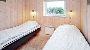 A small, cozy room with wooden walls and a window. There are two single beds with white bedding.