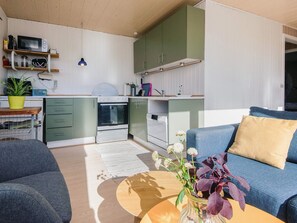 Un espace de vie compact comprenant un coin cuisine, un canapé, une table basse et une plante en pot.