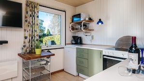 A compact kitchen with a built-in oven, a microwave, and a coffee maker. There is a window with curtains, a potted plant, and a wine bottle on the counter. - Scenic Holiday Home in Hejls near Sea (Hejls)