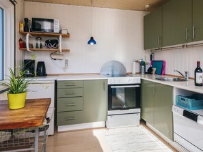 Une cuisine compacte équipée d’un four à micro-ondes, d’une cuisinière et d’un évier. On y trouve une plante en pot sur le comptoir et une petite table.