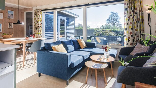 A modern living room with a blue sofa, a black armchair, and a dining area with a table and chairs. - Scenic Holiday Home in Hejls near Sea (Hejls)