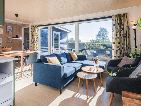 A modern living room with a blue sofa, a black armchair, and a dining area with a table and chairs.