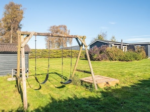 A wooden swing set in a grassy yard with a house and a shed in the background. - Scenic Holiday Home in Hejls near Sea (Hejls)