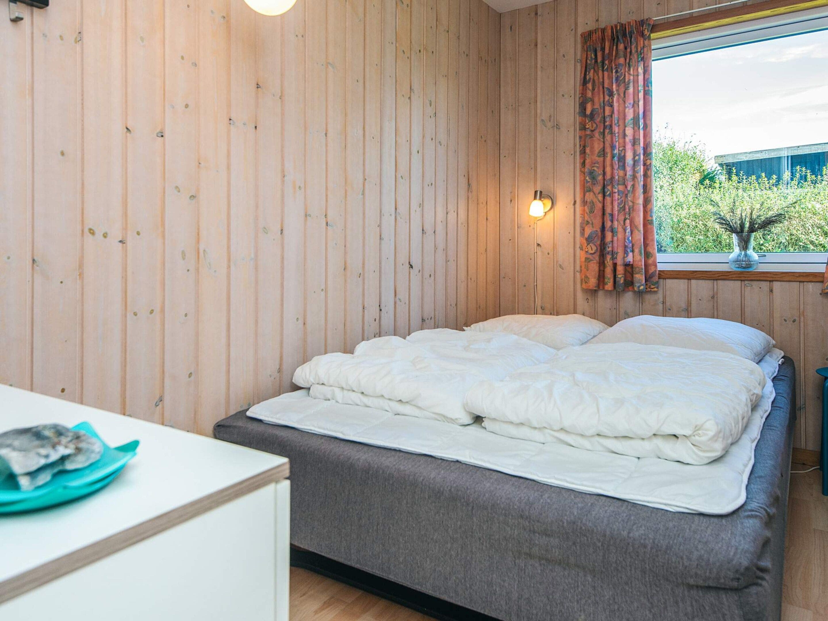A bedroom with a bed, a bedside table, a lamp, and a window with curtains.