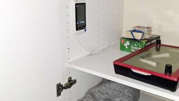 A white room with a small control panel, a red and black object on a table, and a green box with white text.