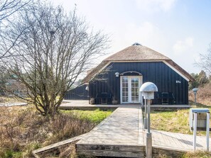 A black building with a thatched roof, a wooden deck leading to the entrance, and a number '57a' on the side.