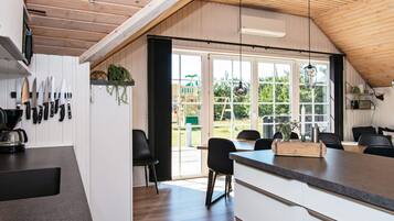 A modern kitchen with a wooden ceiling, large windows, and a dining area with black chairs.