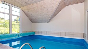 An indoor swimming pool with a wooden ceiling, tiled walls, and a clear view outside.