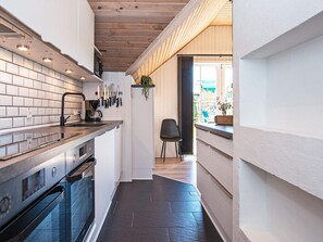 A narrow kitchen with a wooden ceiling, white tiled backsplash, and a black countertop. - 4 Star Holiday Home in Fano (Fano)