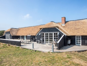 A building with thatched roofs, large windows, and a wooden deck. - 4 Star Holiday Home in Fano (Fano)