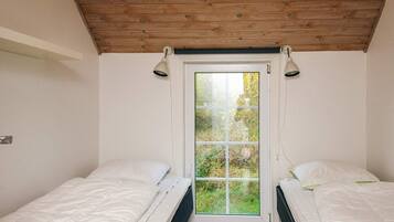 A bedroom with two single beds, a wooden ceiling, and a window with a view of greenery.
