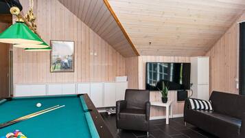 A pool table with balls, a sofa, a chair, a small table with a plant, and a television on the wall.