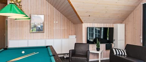A pool table with balls, a sofa, a chair, a small table with a plant, and a television on the wall.
