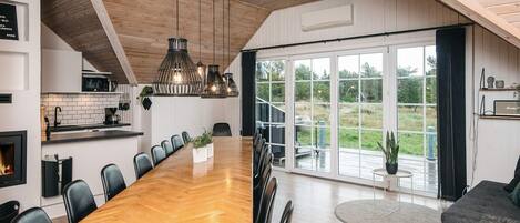 A spacious dining area with a long wooden table, black chairs, and hanging pendant lights.