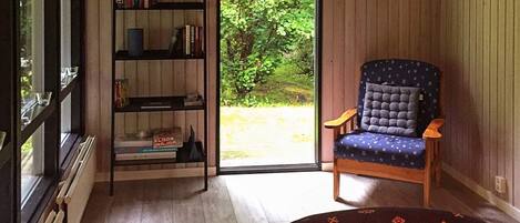 Ein Zimmer mit Holzboden, einer Bücherwand, einem blau gepolsterten Sessel und Blick auf Grünflächen.