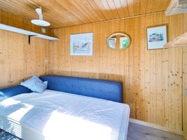 A room with wooden walls, a bed with a blue headboard, a white mattress, and a ceiling fan.