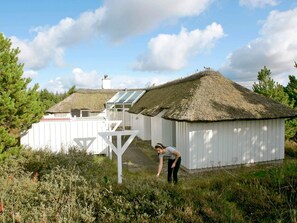 A thatched-roof building with a white exterior, a glass extension, and a person bending over the ground. - 8 Person Holiday Home in Fjerritslev-by Traum (Fjerritslev)