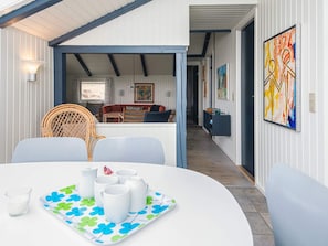 Un coin repas avec une table dressée pour quatre personnes, une chaise en osier, un canapé et un tableau accroché au mur.