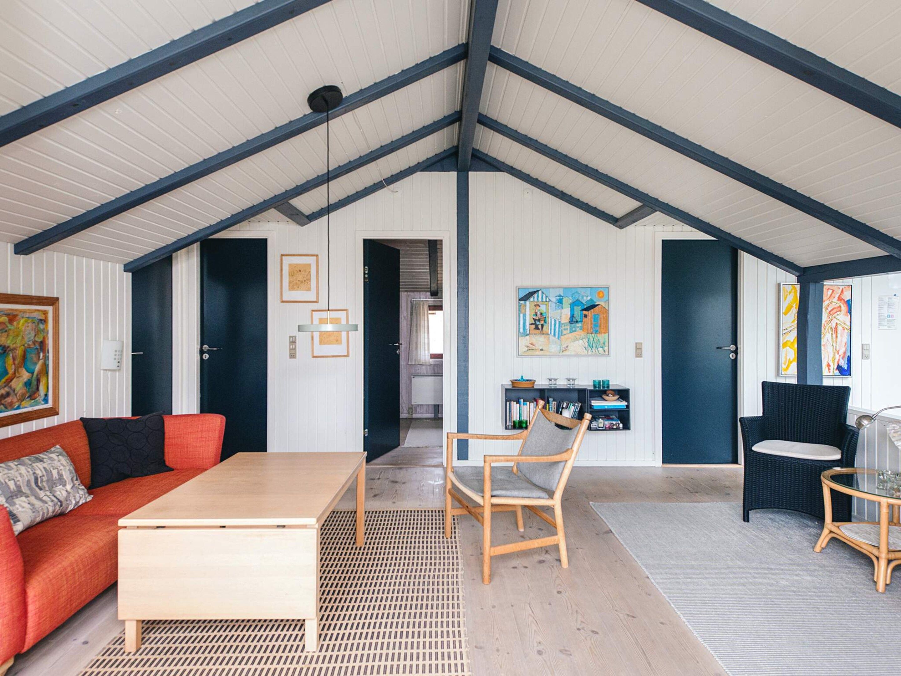 Una habitación amplia con techo alto, una mesa de centro de madera, un sofá rojo, una silla de mimbre y una mesa de vidrio.