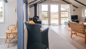 A cozy interior with wicker furniture, a fireplace, and large windows offering a view of the outdoors. - 4 Star Holiday Home in Vejers Strand (Vejers Strand)