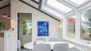 A dining area with a round table, four chairs, a painting, and a view through large windows. - 4 Star Holiday Home in Vejers Strand (Vejers Strand)