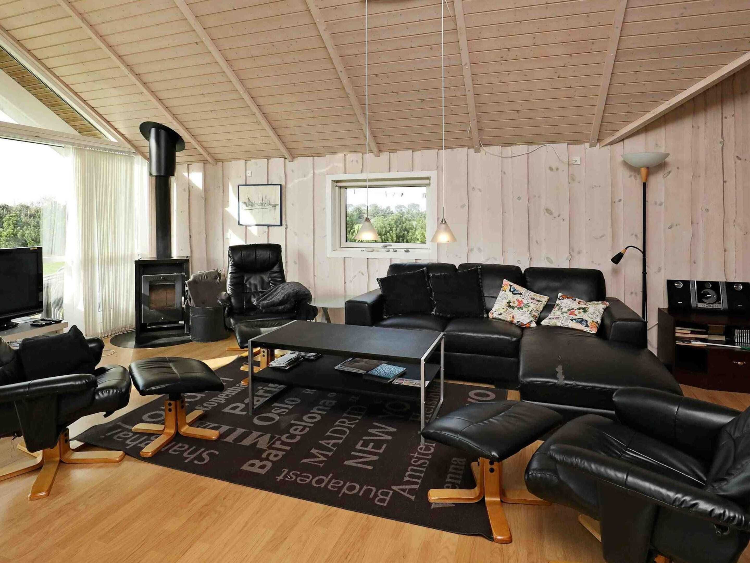A cozy living room with a fireplace, leather furniture, a flat-screen TV, and a view of greenery outside.