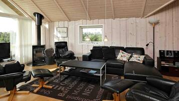 A cozy living room with a fireplace, leather furniture, a flat-screen TV, and a view of greenery outside.