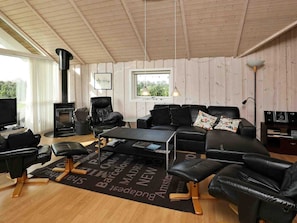 A cozy living room with a fireplace, leather furniture, a flat-screen TV, and a view of greenery outside. - 10 Person Holiday Home in Vaeggerlose (Vaeggerlose)