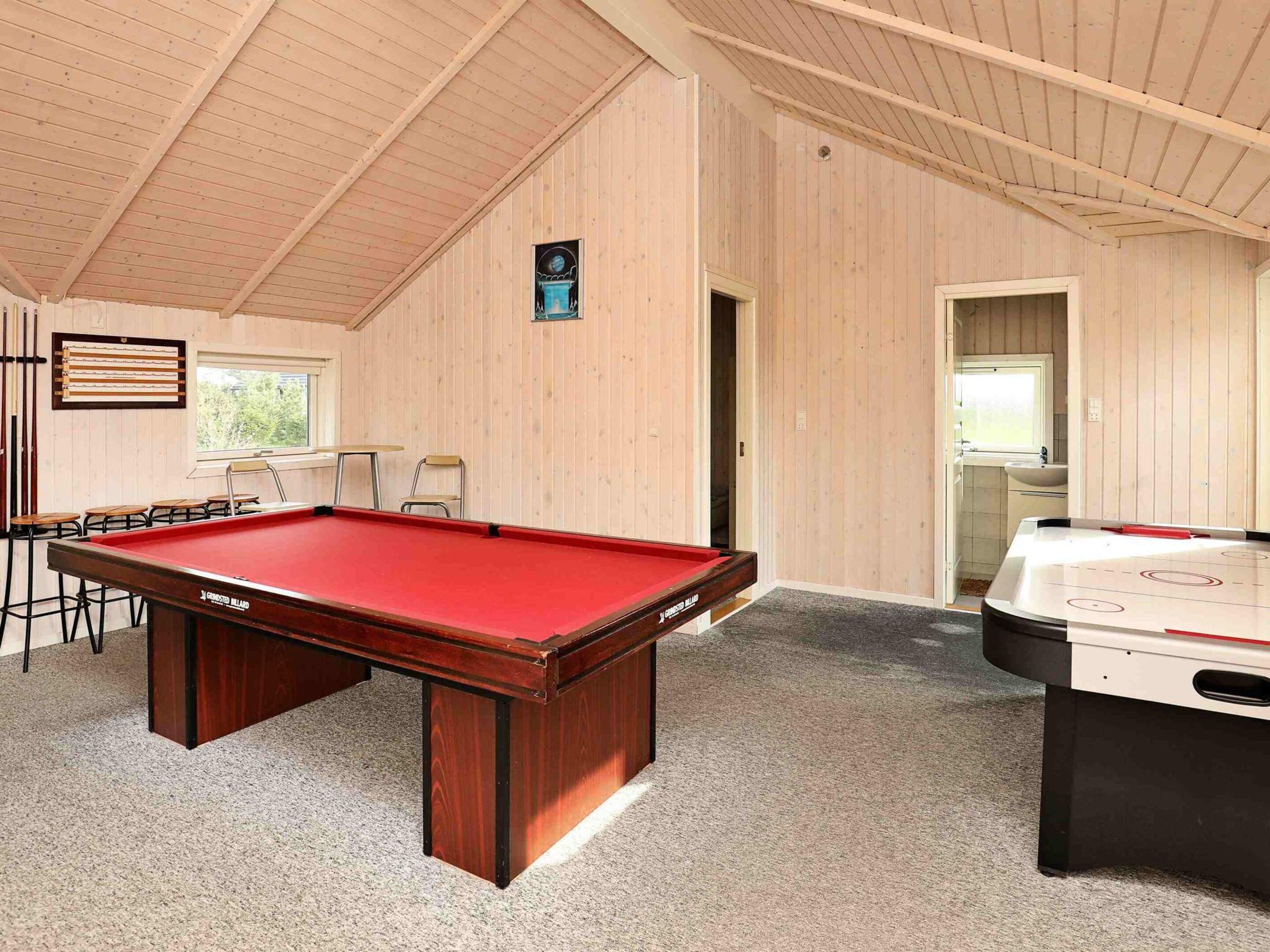 A pool table with a red felt top, a foosball table, and a seating area with chairs and a table.