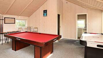 A pool table with a red felt top, a foosball table, and a seating area with chairs and a table.