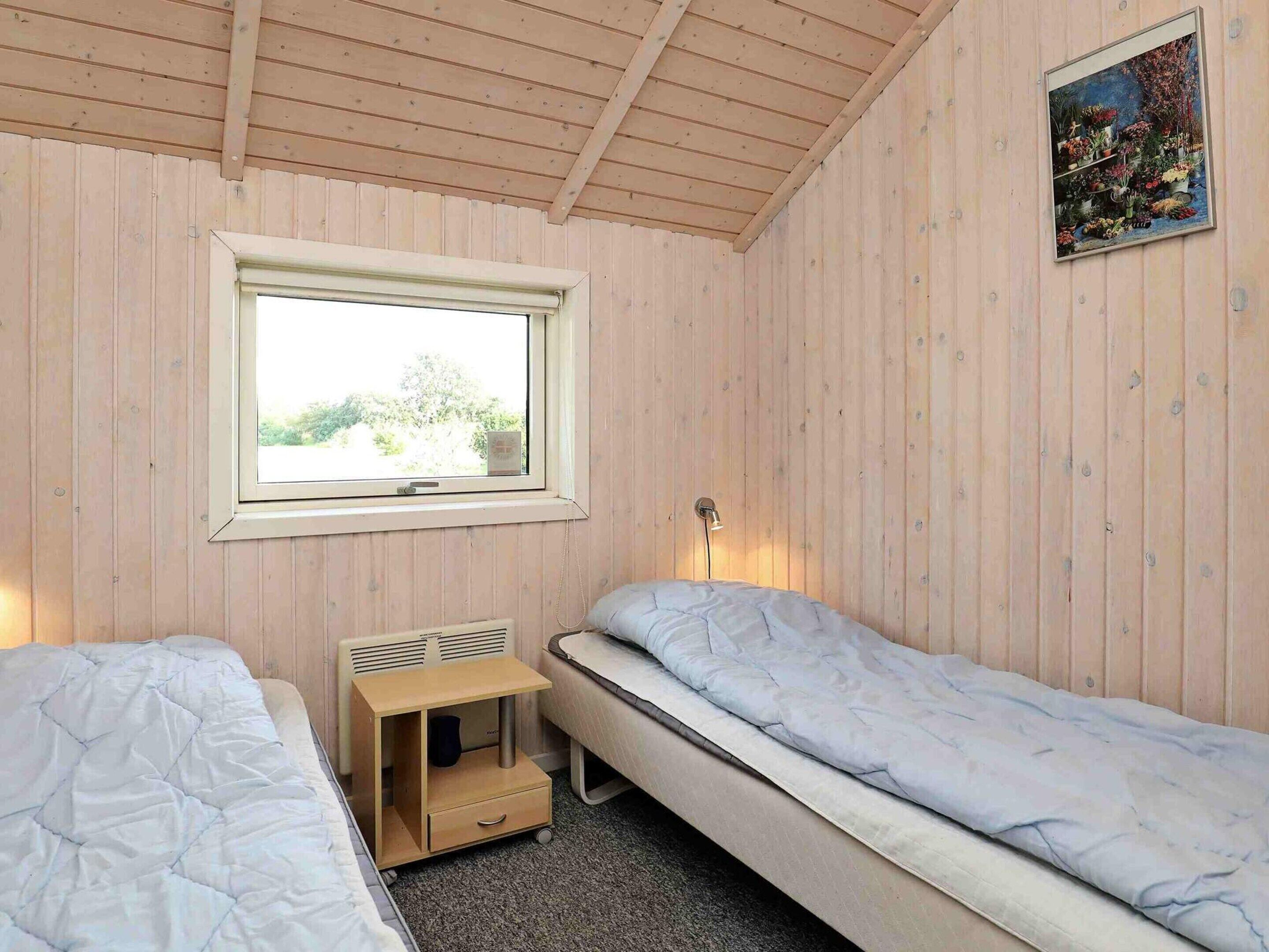 A room with two single beds, a window, a radiator, and a small wooden cabinet.