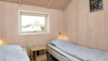 A room with two single beds, a window, a radiator, and a small wooden cabinet.