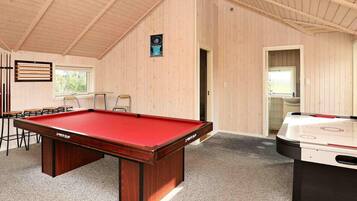 A pool table with a red felt top, a foosball table, and a seating area with chairs and a table.