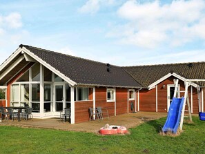 Une maison avec une grande baie vitrée, une terrasse en bois et un toboggan.