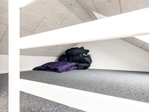 Una escalera con barandilla blanca que conduce a un rellano donde hay una bolsa negra y un objeto morado en el suelo.