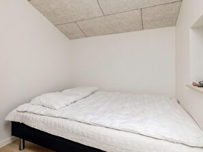 Una cama individual con colchón y almohadas blancos, cabecera negra y repisa con adornos.