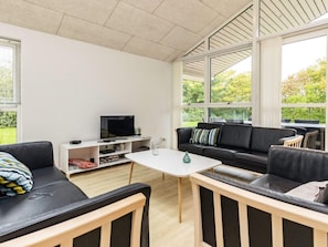 Una sala de estar moderna con un televisor de pantalla plana, un sofá, una mesa de centro y un amplio ventanal con vistas a zonas verdes.