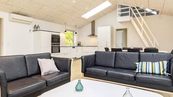 Un salon moderne avec deux canapés en cuir noir, une table basse blanche et un coin cuisine doté de meubles blancs et d’un four encastré.