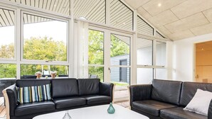 Un salon moderne avec deux canapés en cuir noir, une table basse blanche et de grandes fenêtres donnant sur un paysage verdoyant.