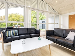 Un salon moderne avec deux canapés en cuir noir, une table basse blanche et de grandes fenêtres donnant sur un paysage verdoyant.