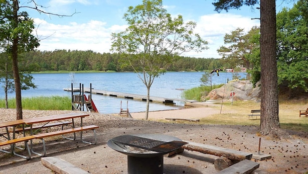 Un camping frente al lago con mesas de picnic, una zona de fogata y un muelle que se adentra en el agua.